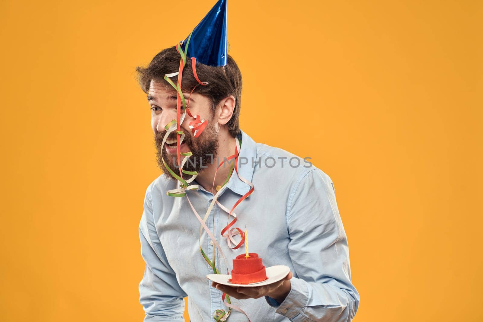 Cheerful man with a cake on a yellow background birthday holidays cap on his head by SHOTPRIME