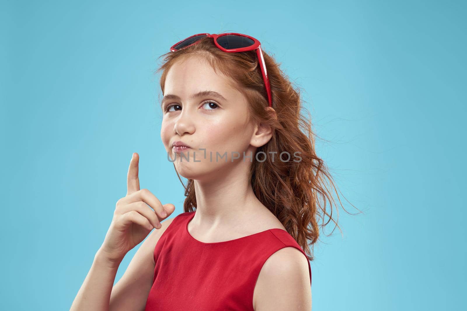 girl with curly hair sunglasses red dress and childhood fun blue background. High quality photo