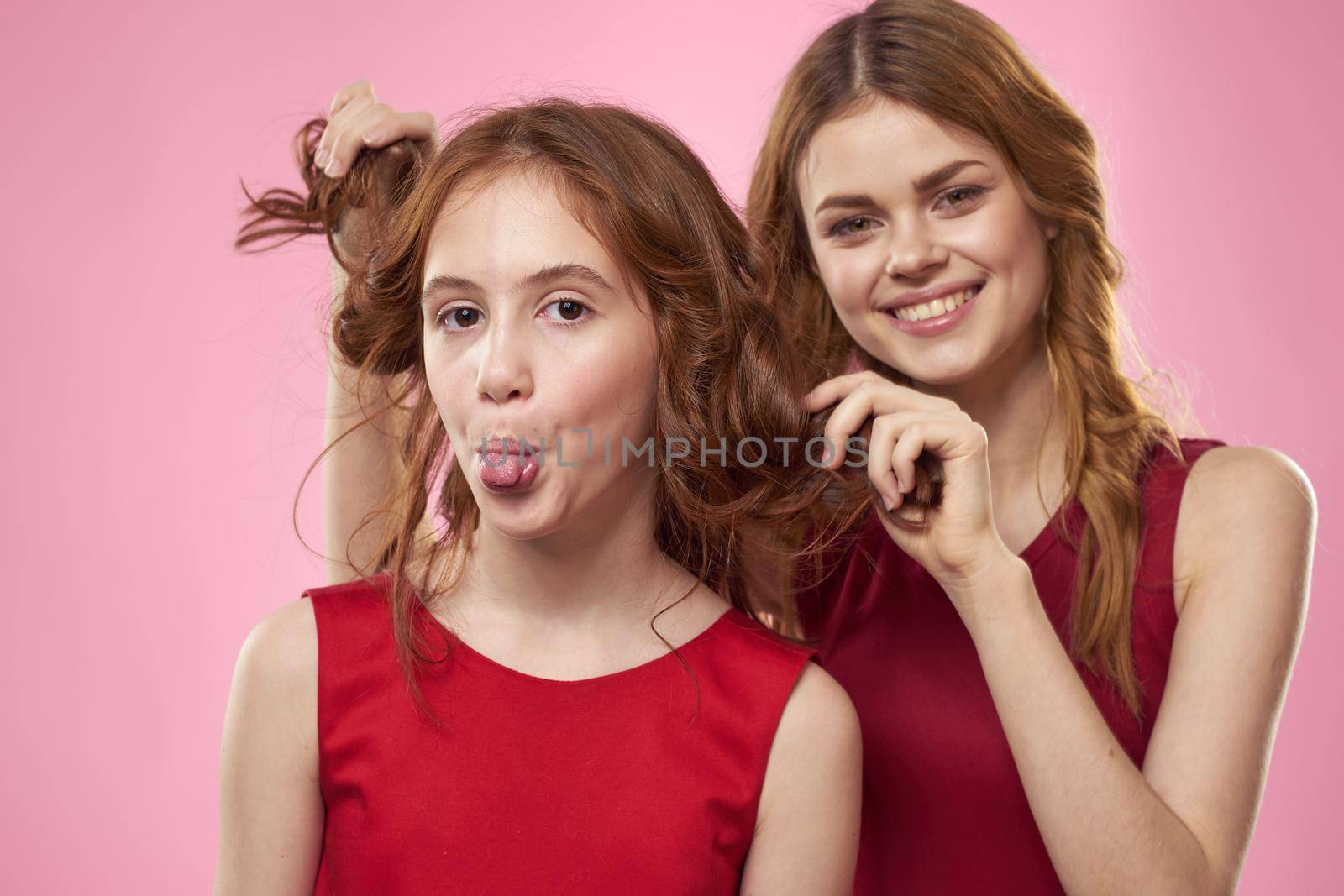 Mom and daughter in red dresses hugs fun grimace childhood joy pink background. High quality photo