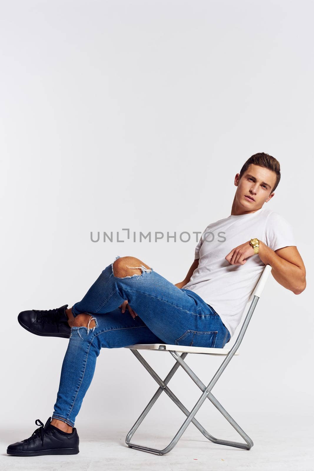 a man in jeans and a t-shirt sits on a chair on a light background side view. High quality photo
