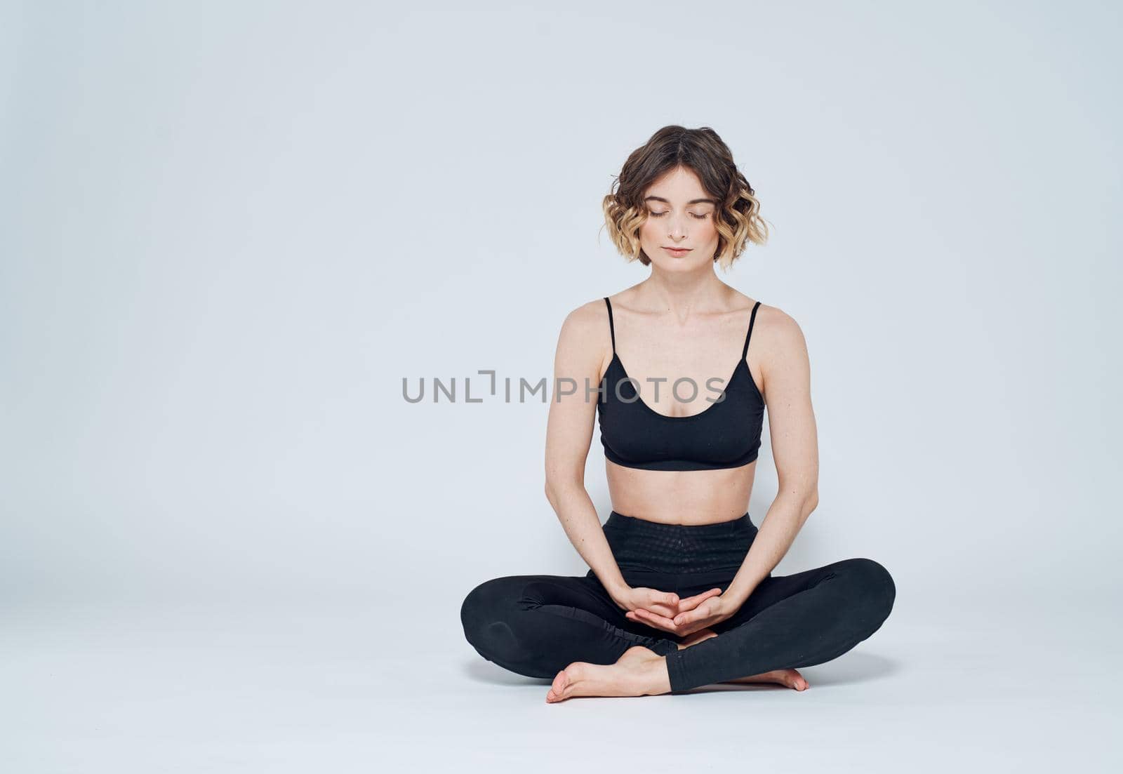 A woman is meditating on a light background with her legs crossed on the floor by SHOTPRIME