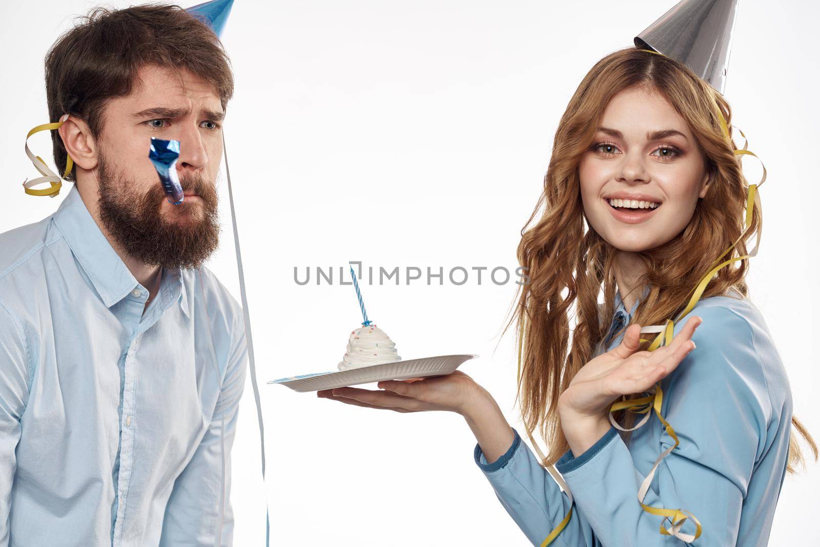 energetic man and woman with a cake and in hats celebrate a birthday on a light background by SHOTPRIME