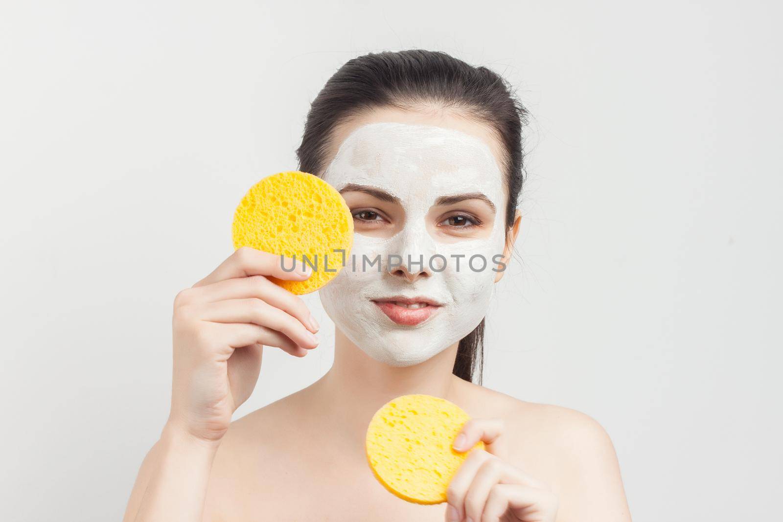 emotional brunette with bare shoulders removing cream from face with sponges. High quality photo