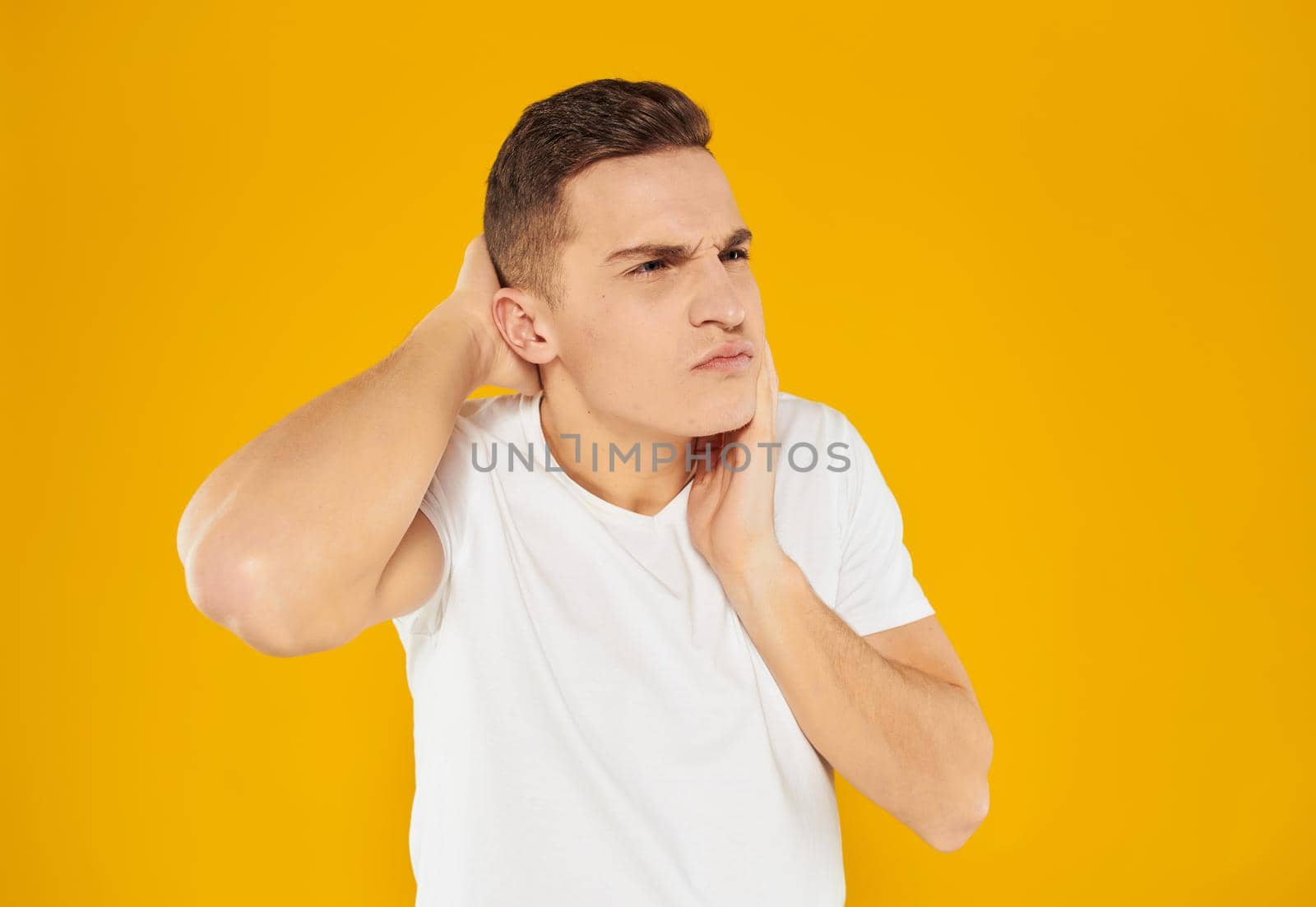 A man in a white T-shirt touches his face with his hand on a yellow background of emotion by SHOTPRIME