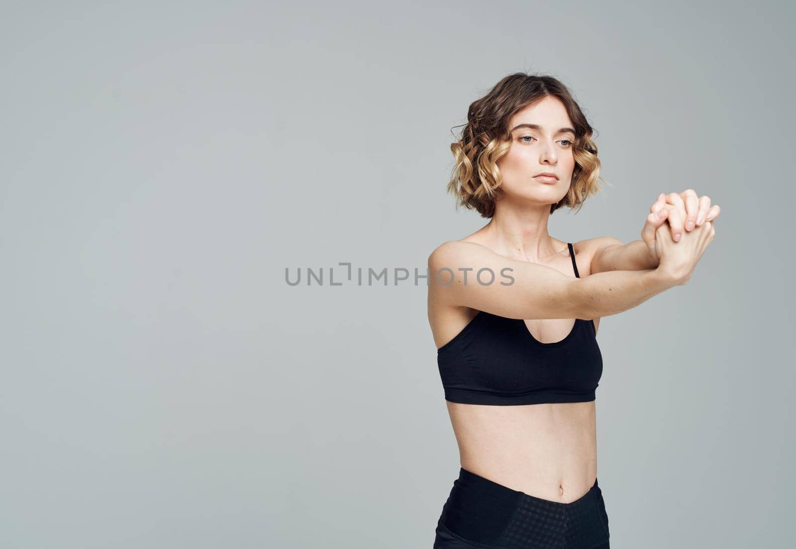 A woman in a short T-shirt on a gray background gestures with her hands to her bare shoulders Fitness Yoga asana. High quality photo