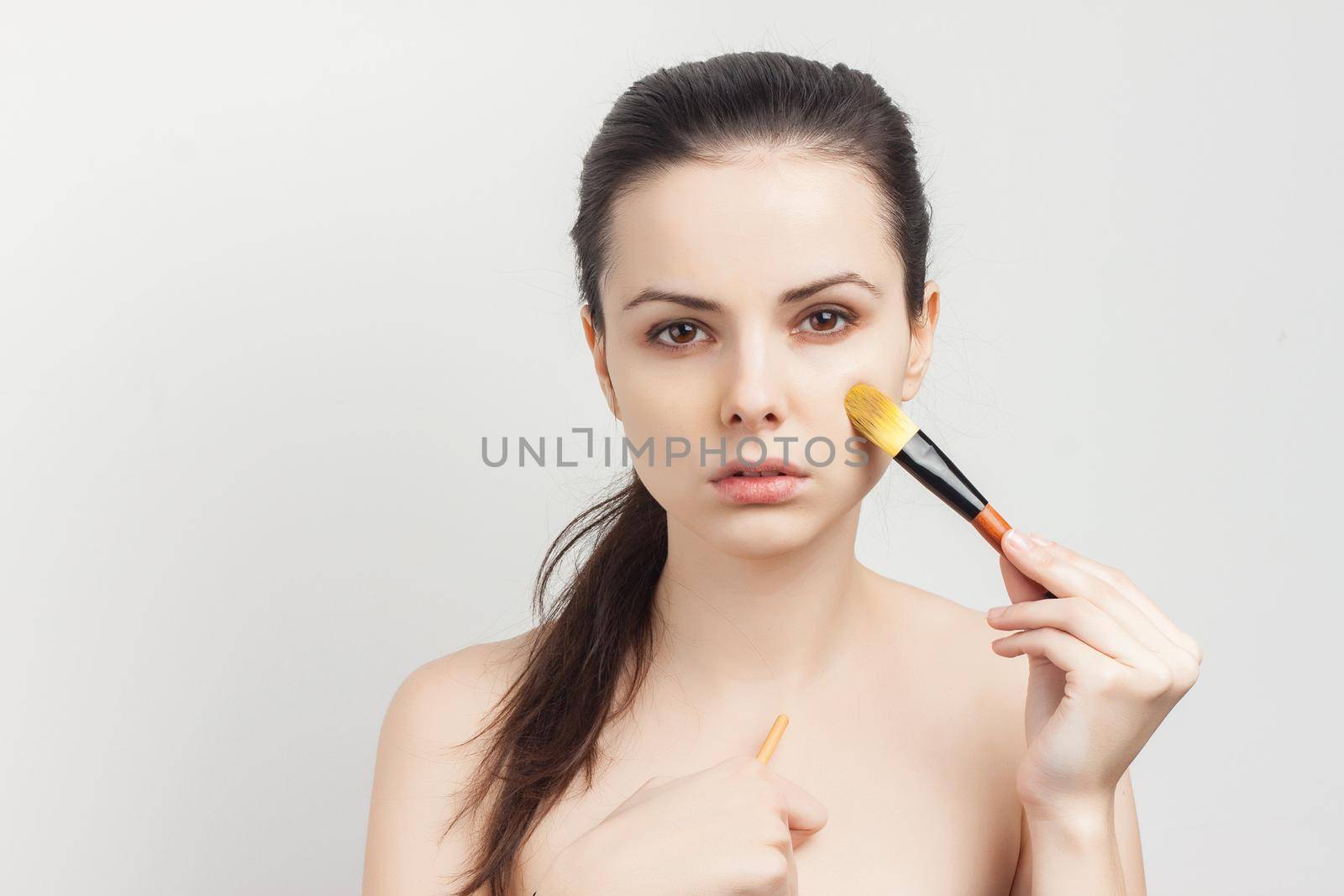 pretty woman with bare shoulders brush in hand skin care applying makeup. High quality photo
