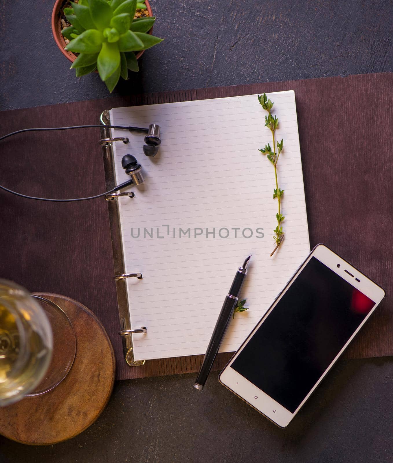 Opened notepad with blank area for text or message, pen, small earphone, smart phone, on wood table