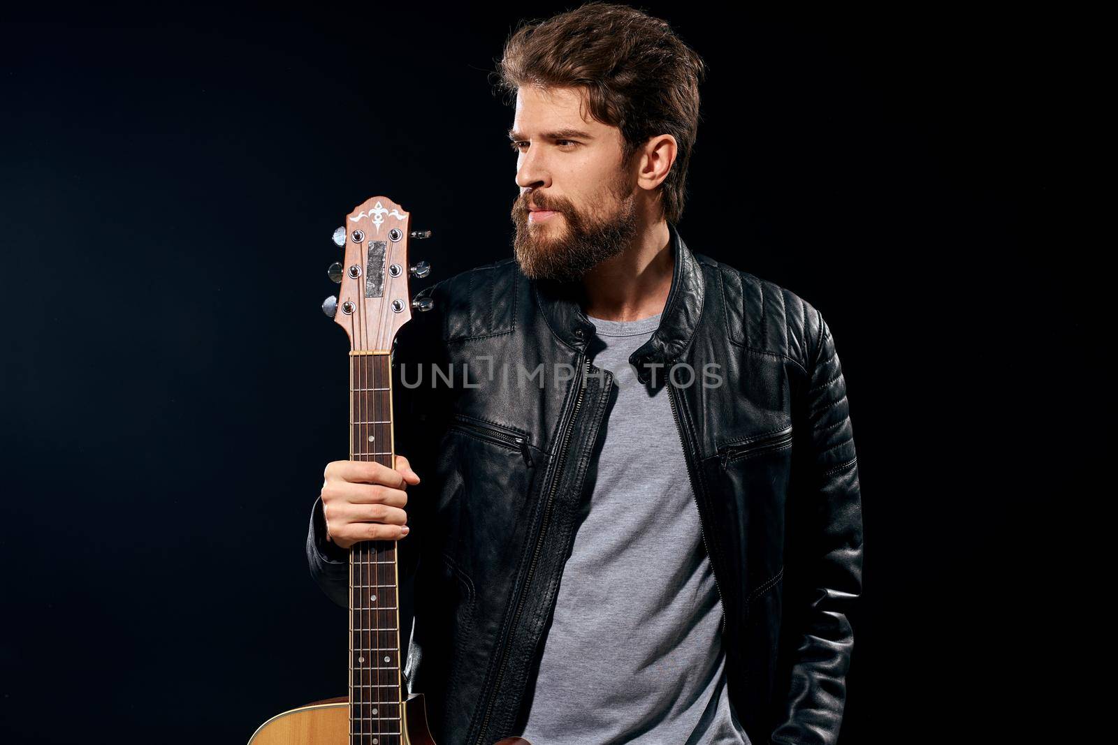 A man with a guitar in his hands leather jacket music performance rock star modern style dark background. High quality photo