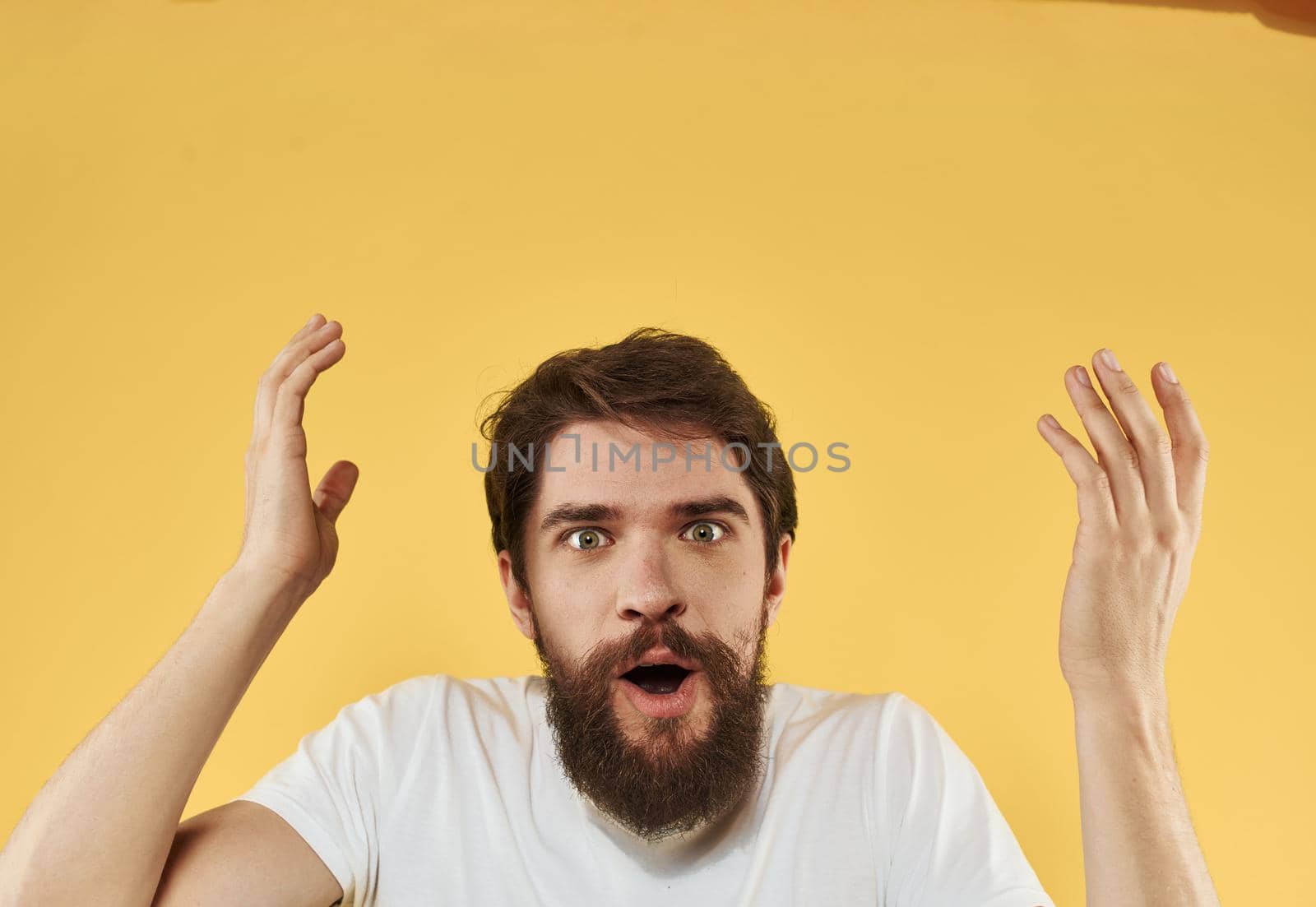 Emotional guy in a white t-shirt on a yellow background gesturing with his hands cropped view. High quality photo