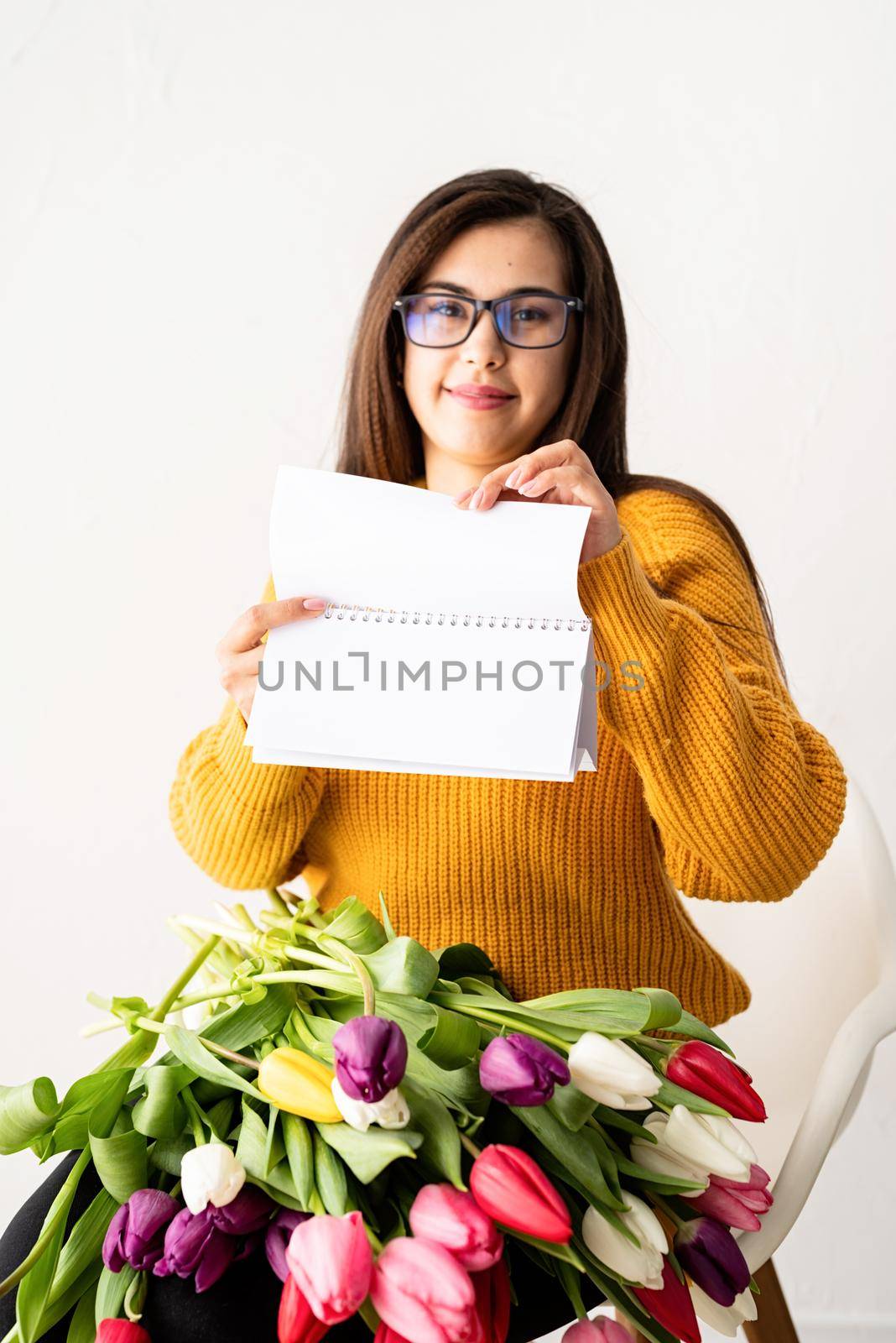 Beautiful young brunette woman with bouquet of fresh pink tulips and blank calendar for mock up by Desperada