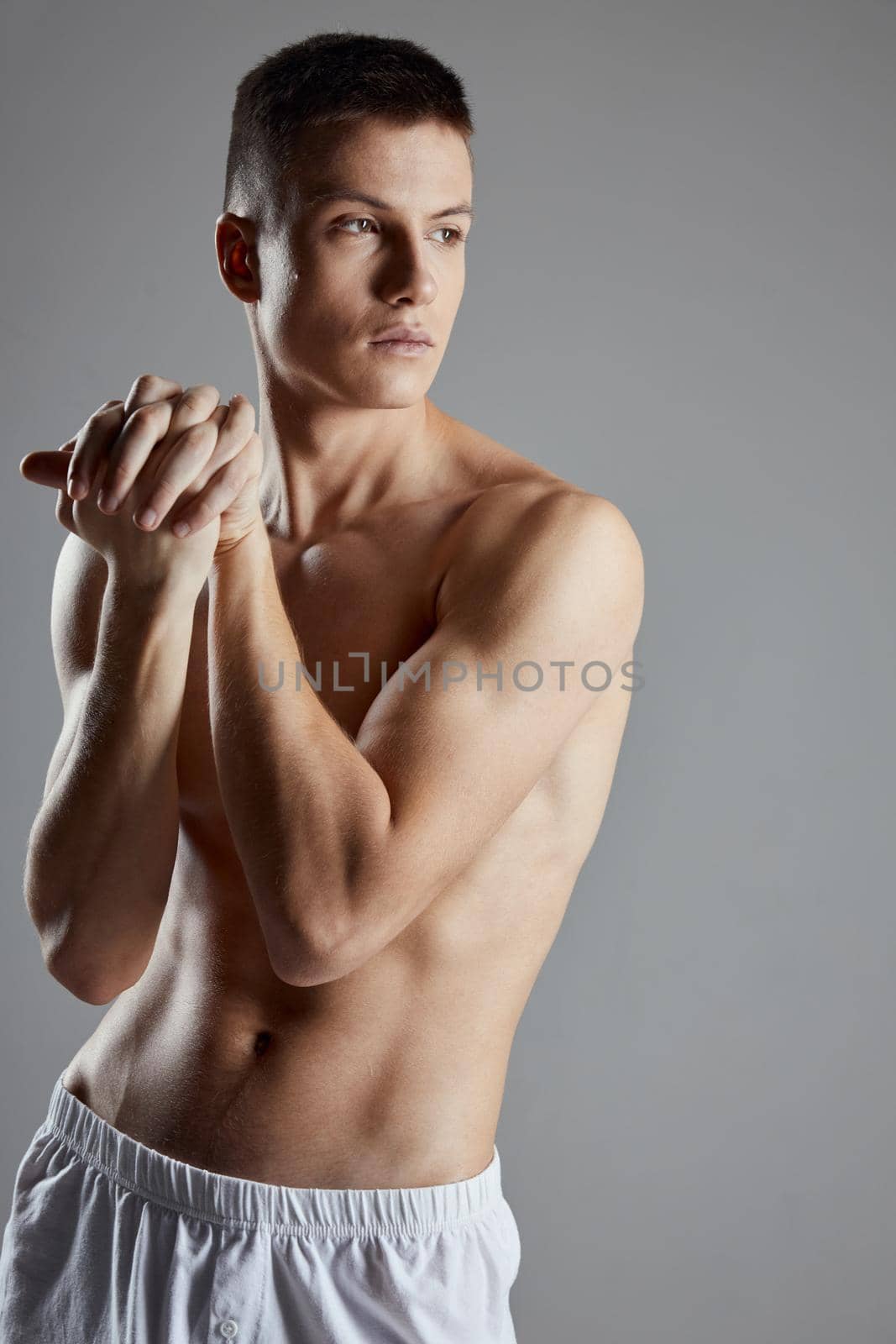 guy with athletic physique joined hands near shoulder on gray background. High quality photo