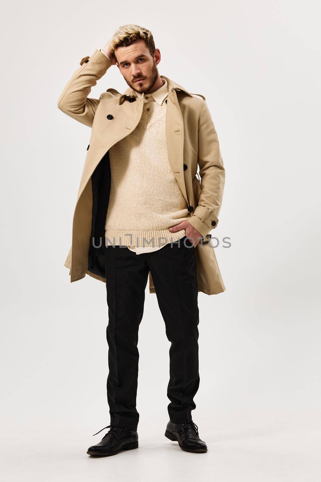 man in beige coat holds his hand behind his head fashion studio full length by SHOTPRIME