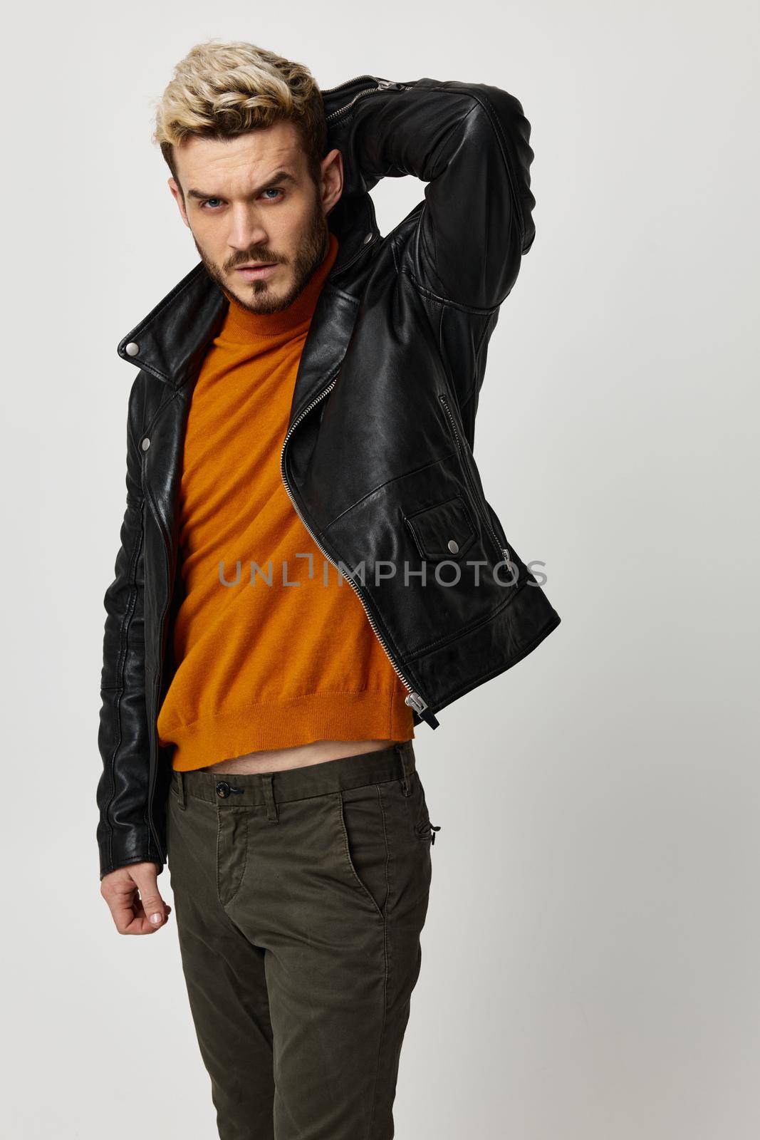 a blond guy in a leather jacket holding his hands behind his head and an orange sweater pants Copy Space by SHOTPRIME