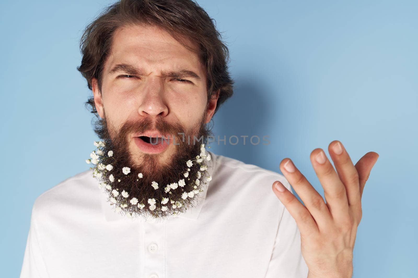 Emotional man in a white T-shirt flowers in a beard close-up blue background. High quality photo