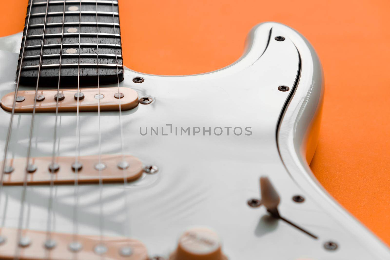 Detail of White Electric Guitar on a orange background.