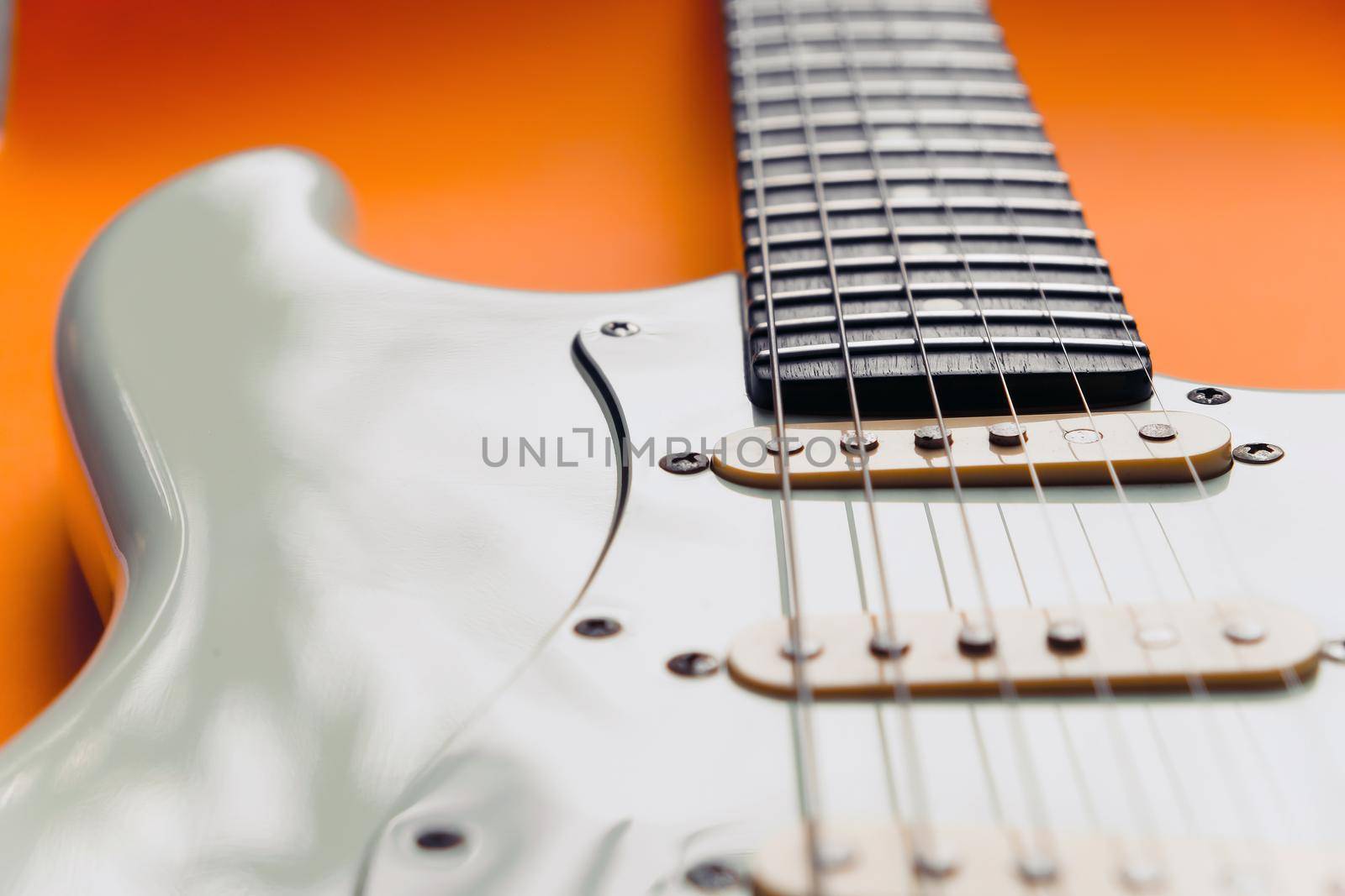 Detail of White Electric Guitar on a orange background.