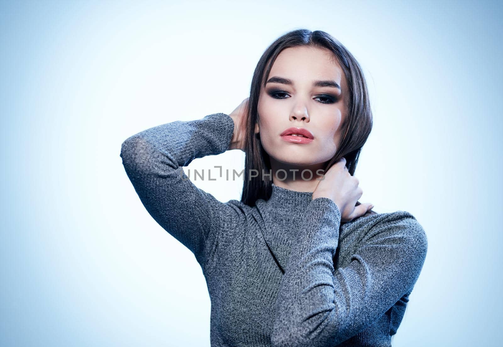 Sexy brunette in a gray sweater on a light background holds her hands behind her head cropped view. High quality photo