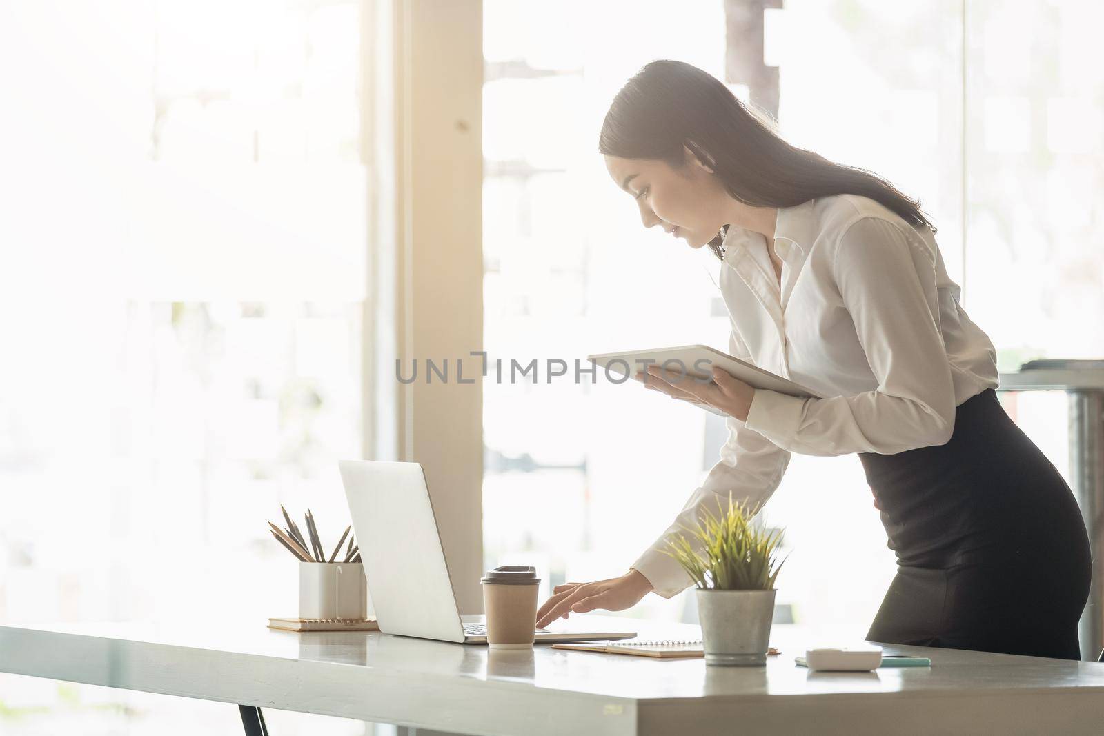Young businesswoman standing at her desk using a laptop - Business Concept