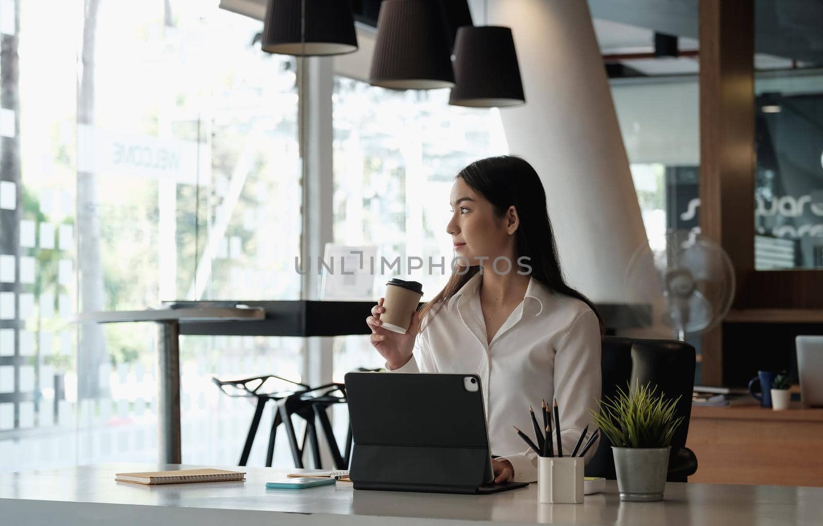 Portrait of beautiful woman or accountant sitting at desk in modern office with interior looking outside enjoying freetime