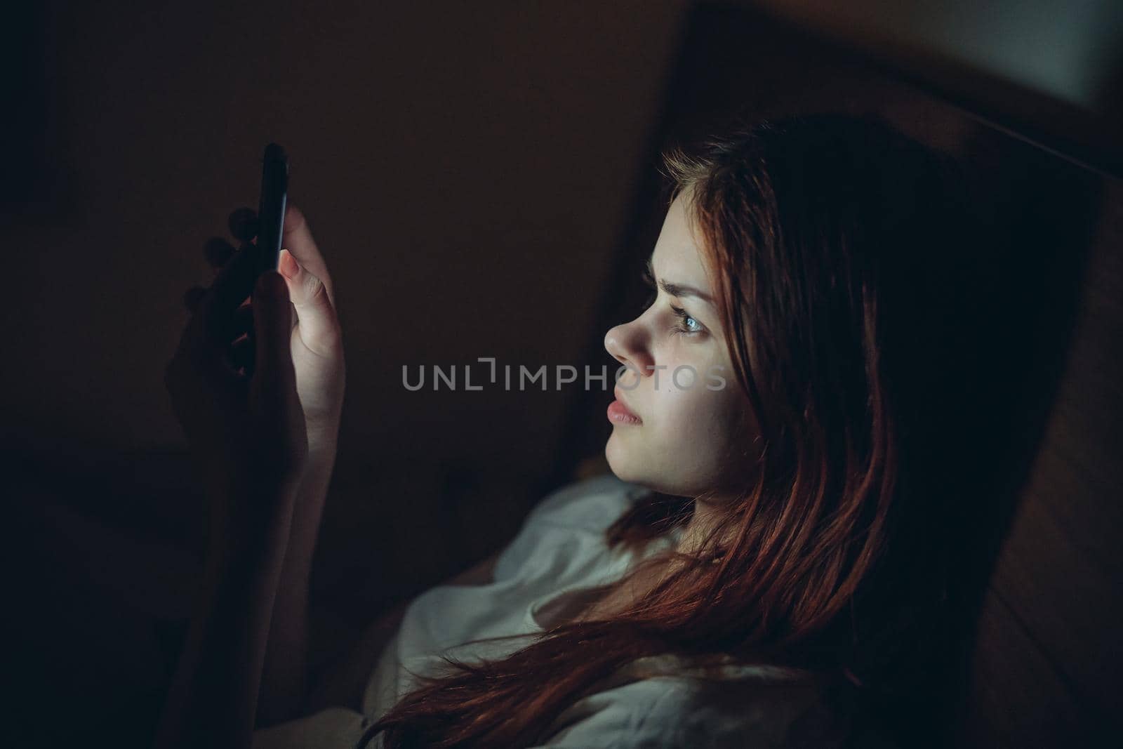 pretty woman lying in bed with phone in hand at night rest before bedtime by SHOTPRIME