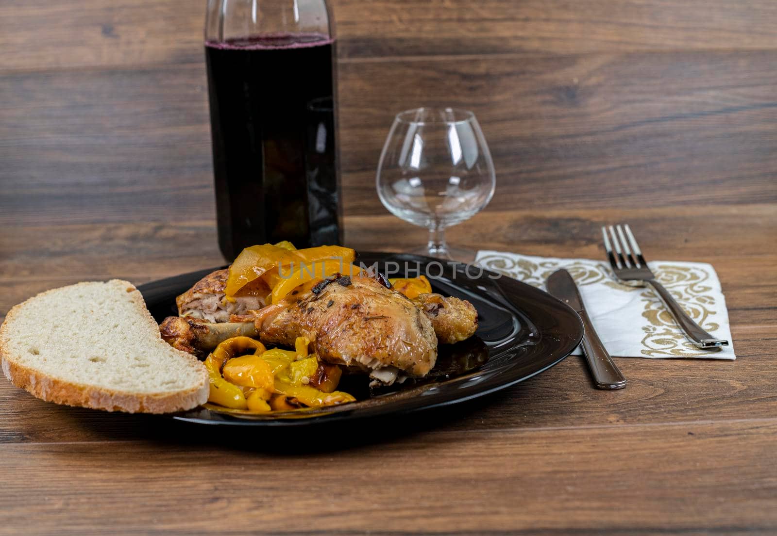 chicken legs and yellow peppers with glass bread and cutlery on black plate wood background