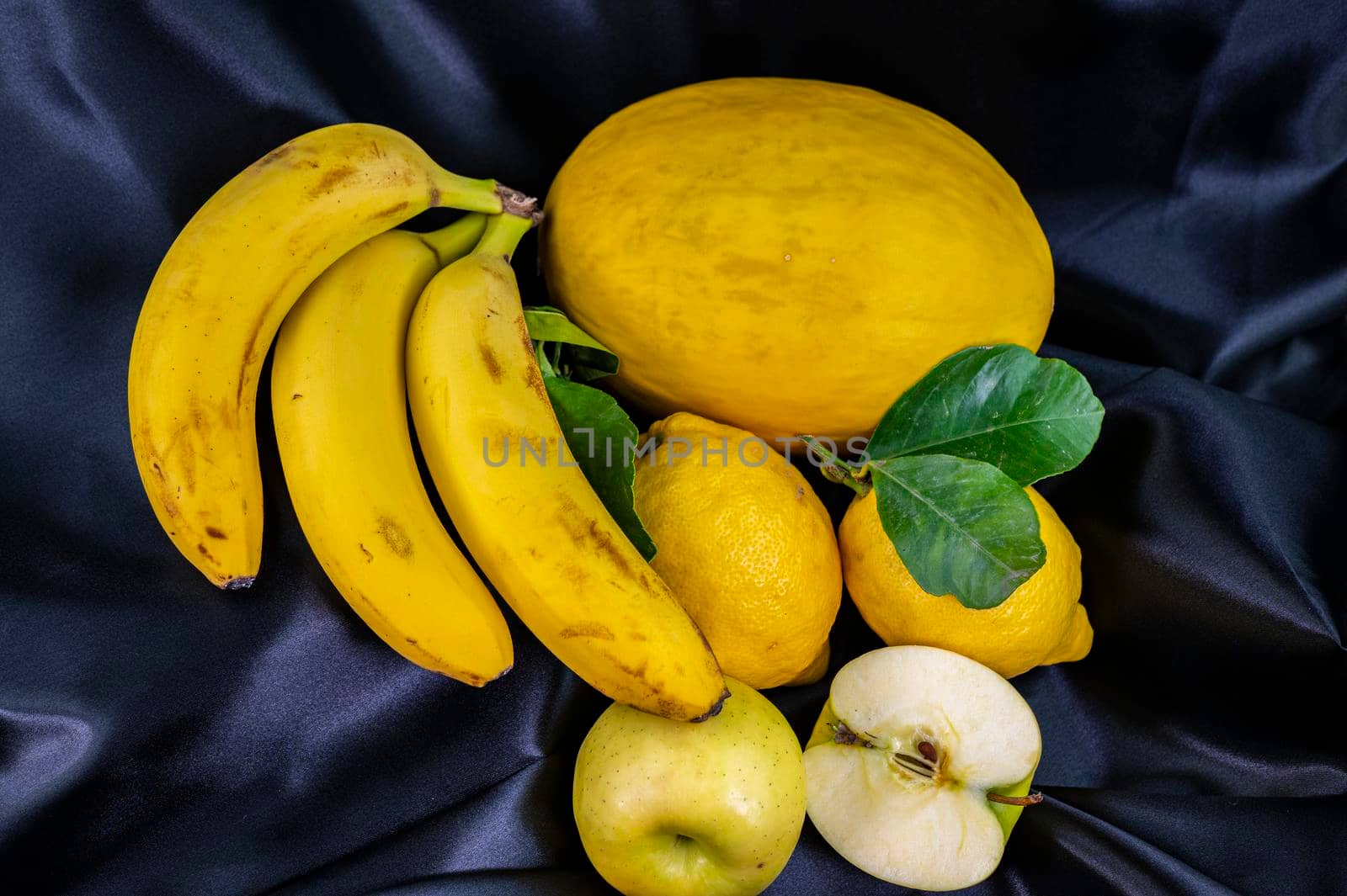 yellow fruit on a black background with melon bananas apples and lemons