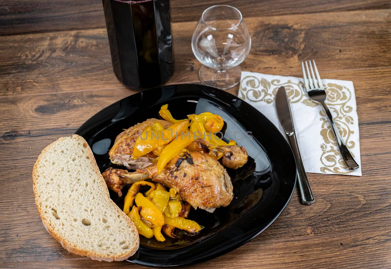 chicken legs and yellow peppers with glass bread and cutlery on black plate wood background