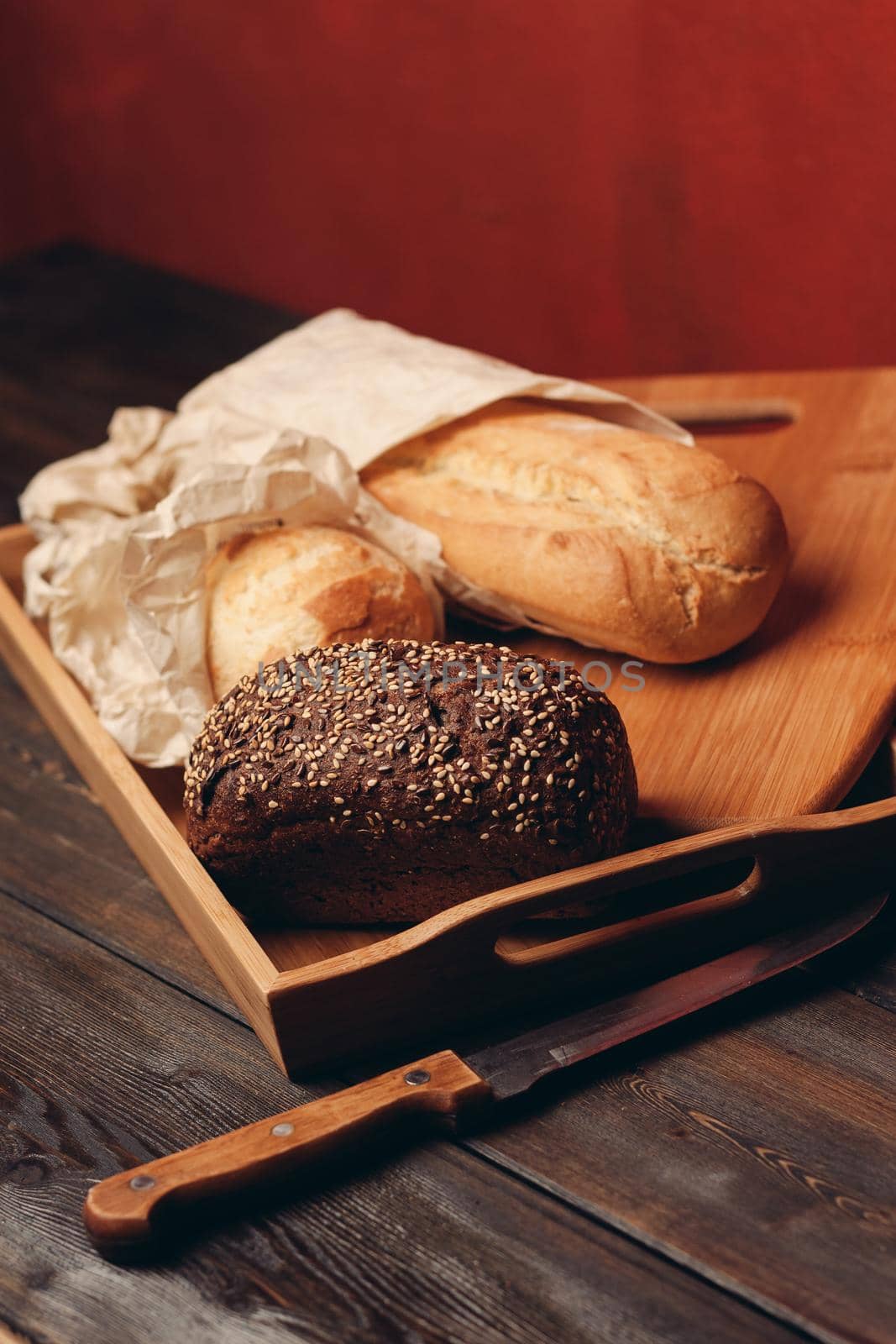 flour products rye bread on a tray and a sharp knife on a table on a red background by SHOTPRIME