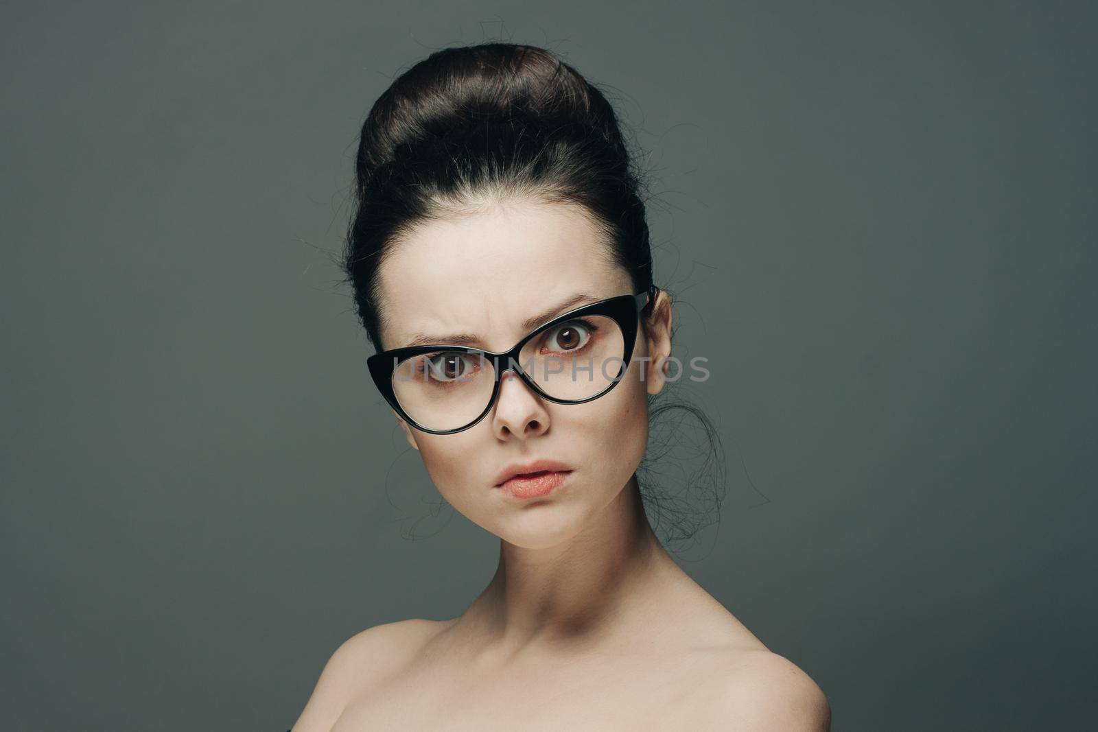 surprised woman with glasses naked shoulders gathered hair gray background by SHOTPRIME