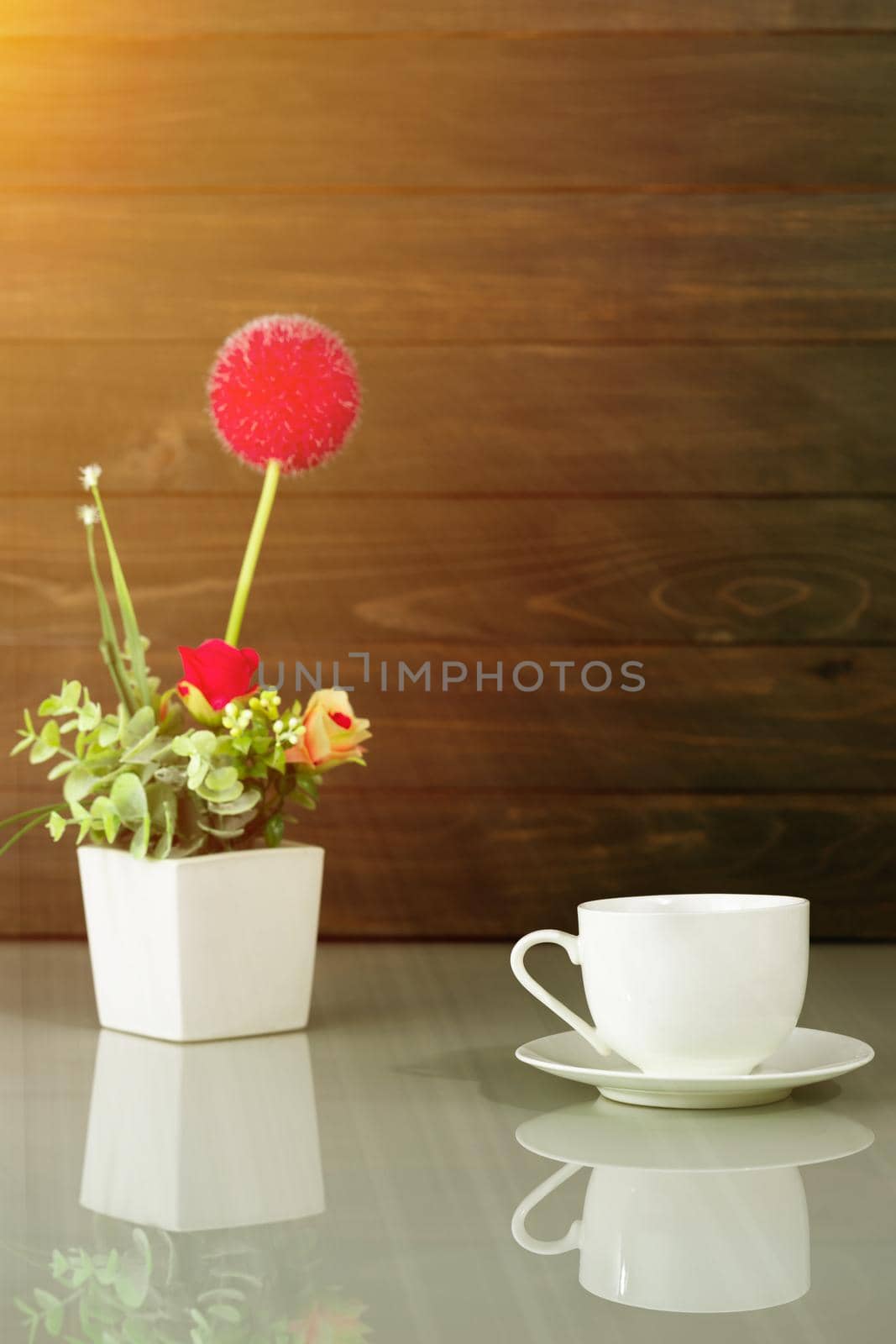 White coffee cup and Artificial flower vase bouquet over table with wood wall background