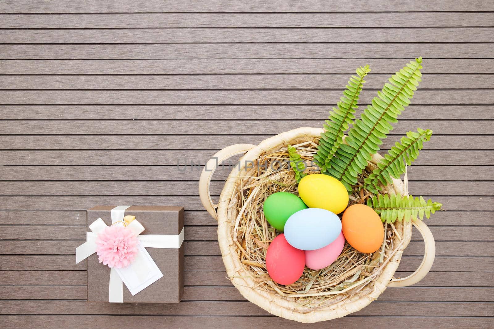 Colorful easter eggs in the basket and gift box on wood background with space