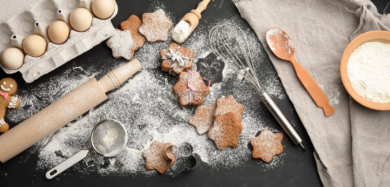 baked star-shaped gingerbread cookie sprinkled with powdered sugar on a black table and ingredients, top view