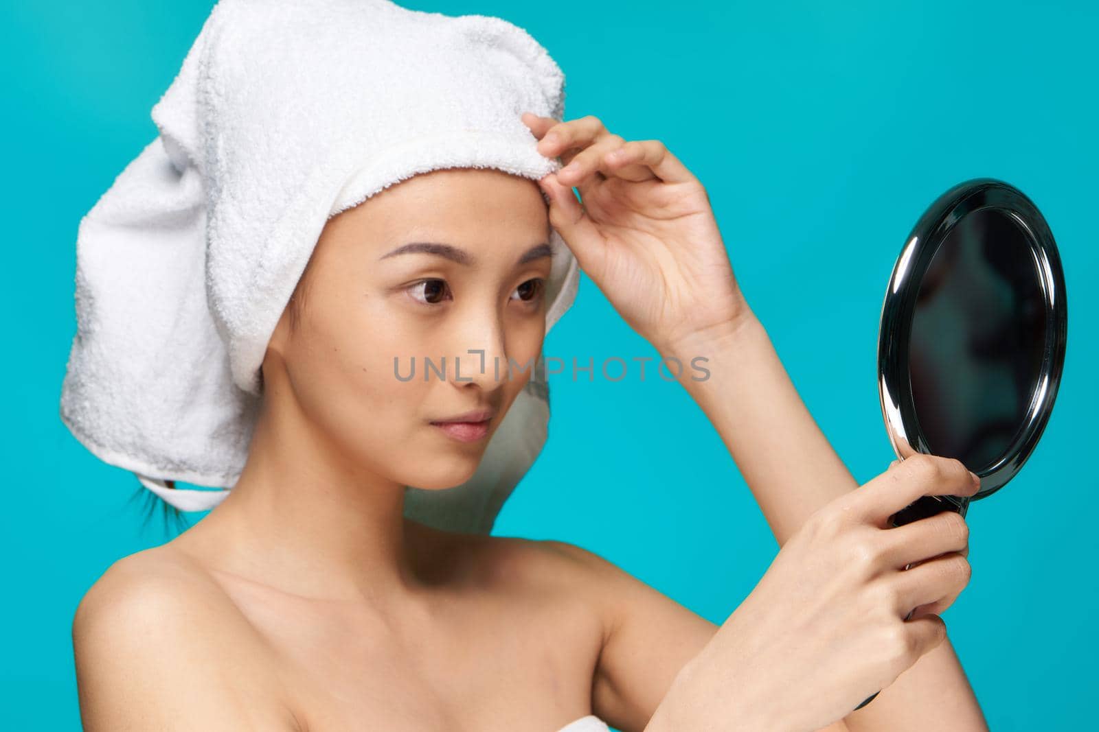 woman of asian appearance naked shoulders mirror in hands clear skin blue background by SHOTPRIME