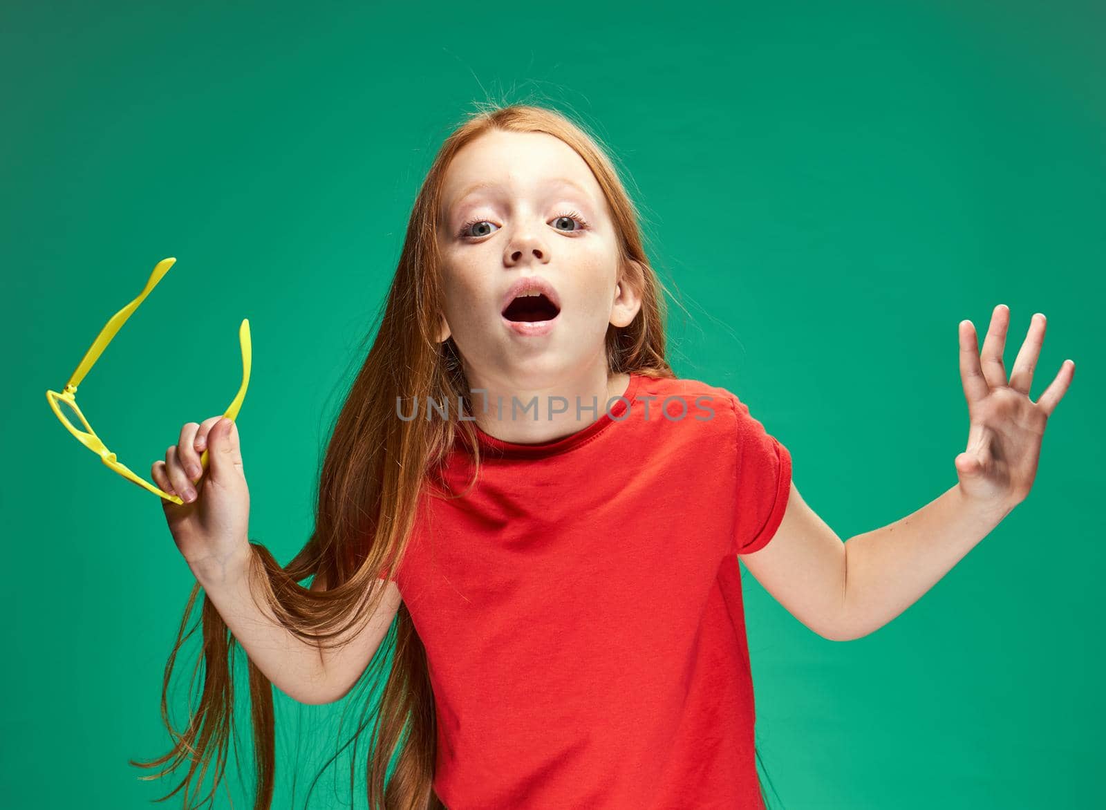 red-haired girl holding glasses in her hands red t-shirt emotions green background. High quality photo