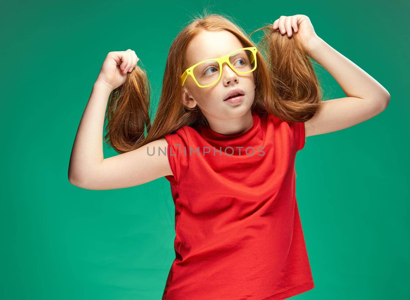 girl in a red T-shirt with loose hair emotions yellow glasses Green background. High quality photo