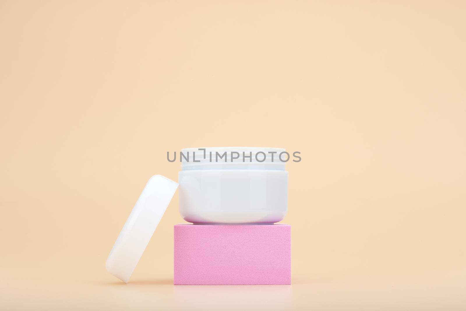 White opened cosmetic jar on pink podium against beige background with copy space. Concept of beauty products for skin care, body care or hair care. Face cream, scrub or mask enriched with natural oil