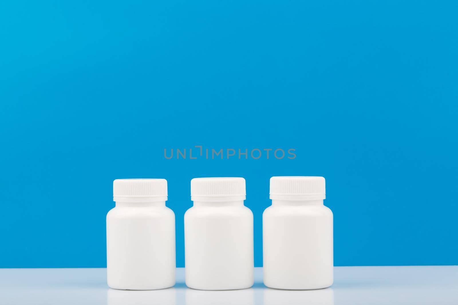 Three white medication bottles on white table against blue background with copy space. Concept of vitamins, supplements, medication and healthcare. High quality photo