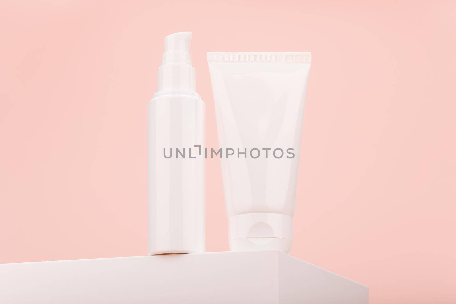 Two white cosmetic tubes on podium shot from epic angle against light pink background with copy space. Concept of skin care and beauty