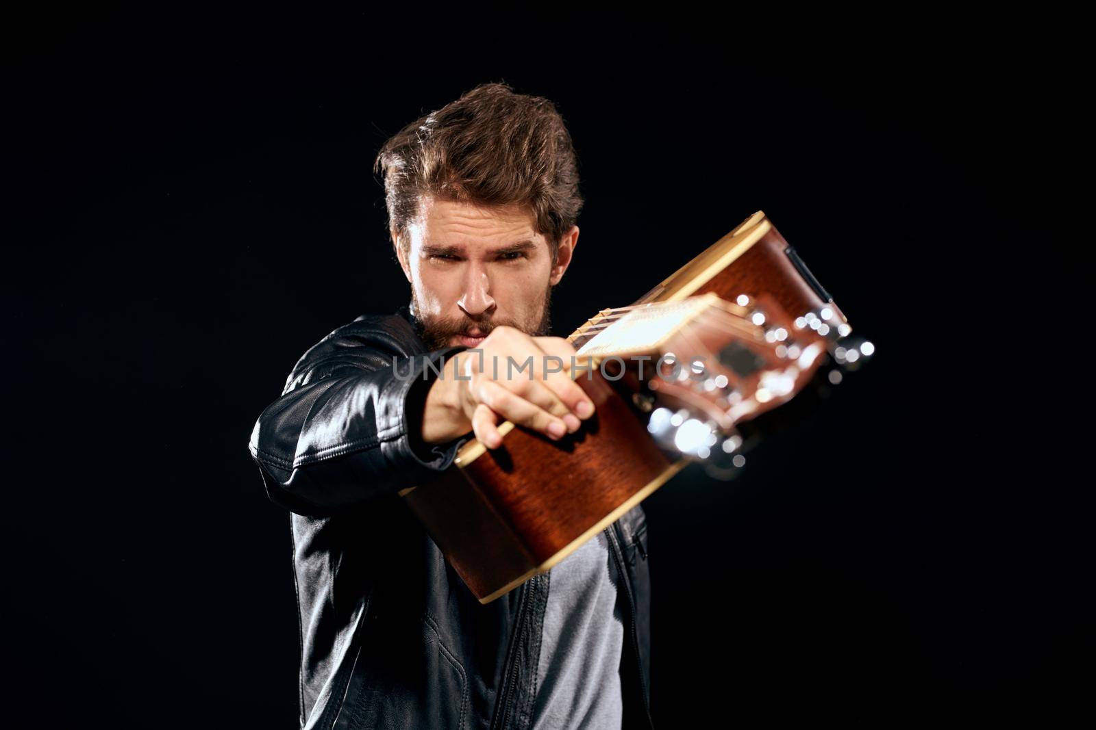 A man with a guitar in his hands leather jacket music performance rock star modern style dark background. High quality photo