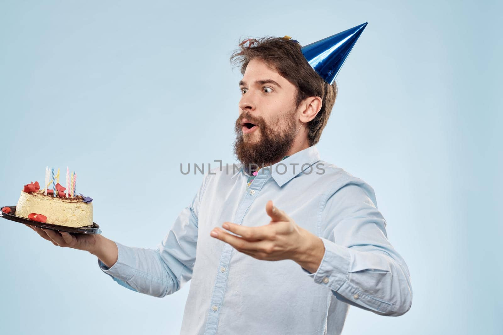 Man with a plate of cake and a festive candle blue background cap corporate party. High quality photo