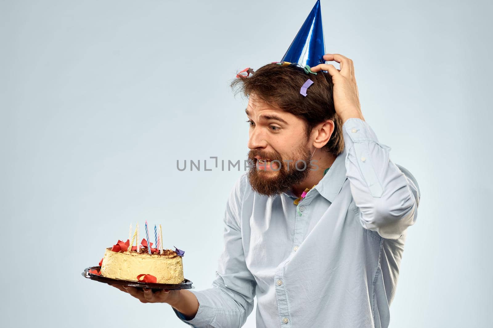 Man with a plate of cake and a festive candle blue background cap corporate party. High quality photo