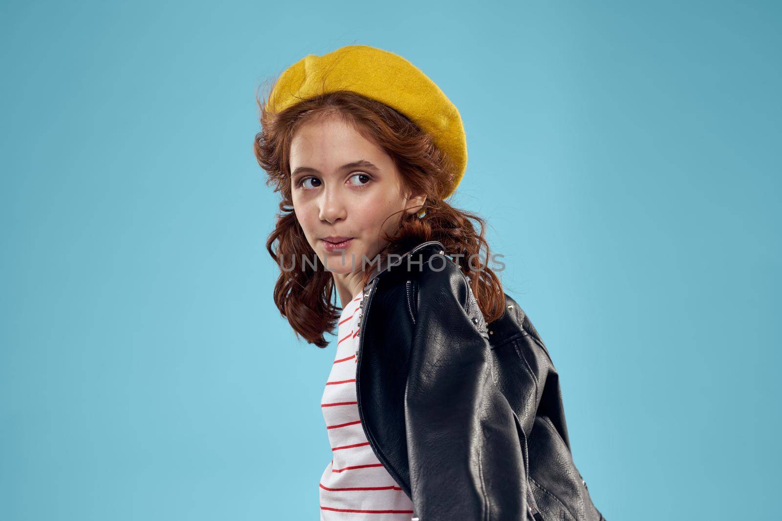 Fashionable girl in a black leather jacket on a blue background and a yellow hat on her head. High quality photo