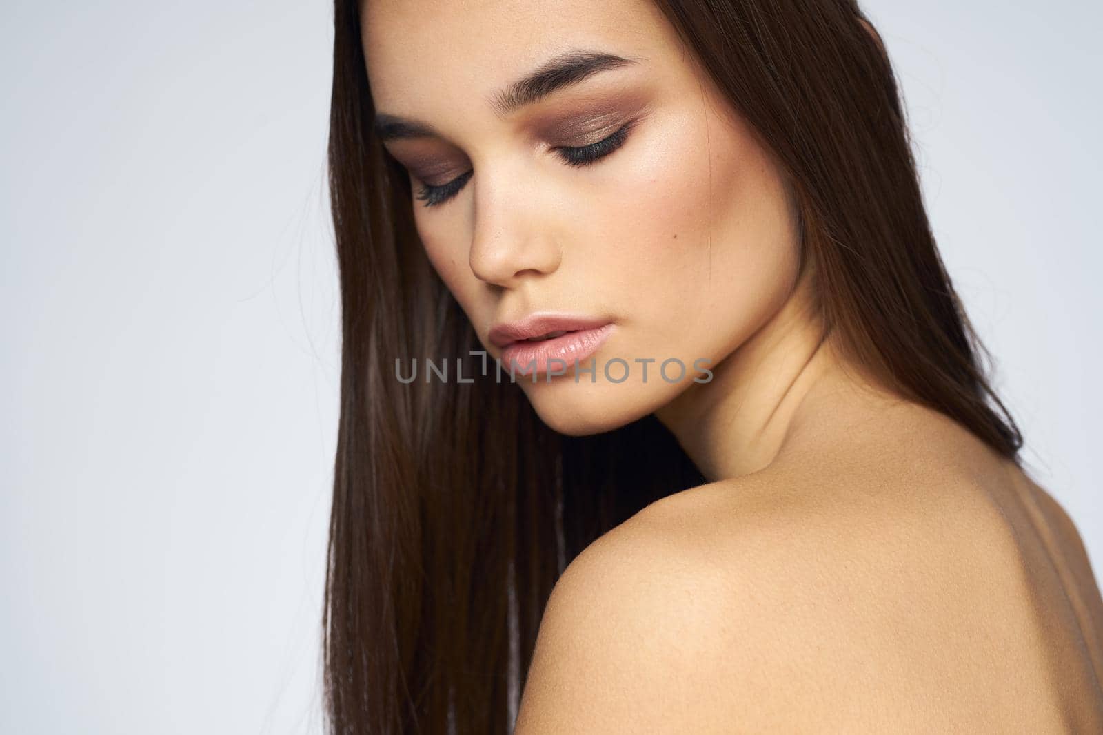 Pretty brunette naked shoulders long hair close-up light background. High quality photo