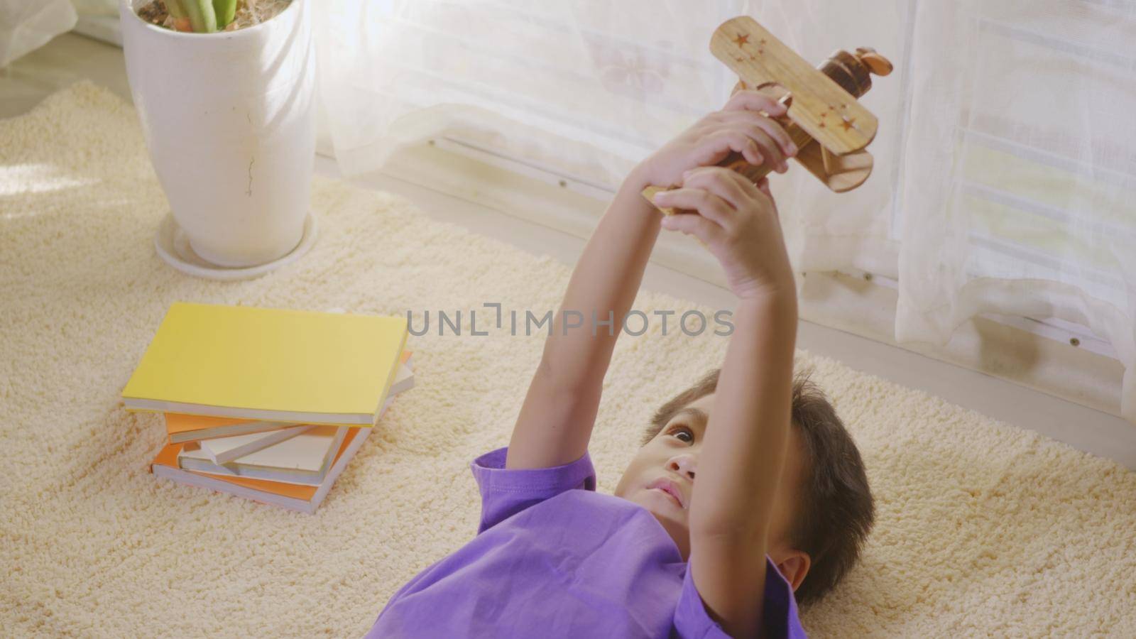 Happy Asian kid boy aircraft pilot child's desire fly high at home on carpet. Funny child's playing with toy passenger wooden plane and dreaming of becoming a pilot. Top view