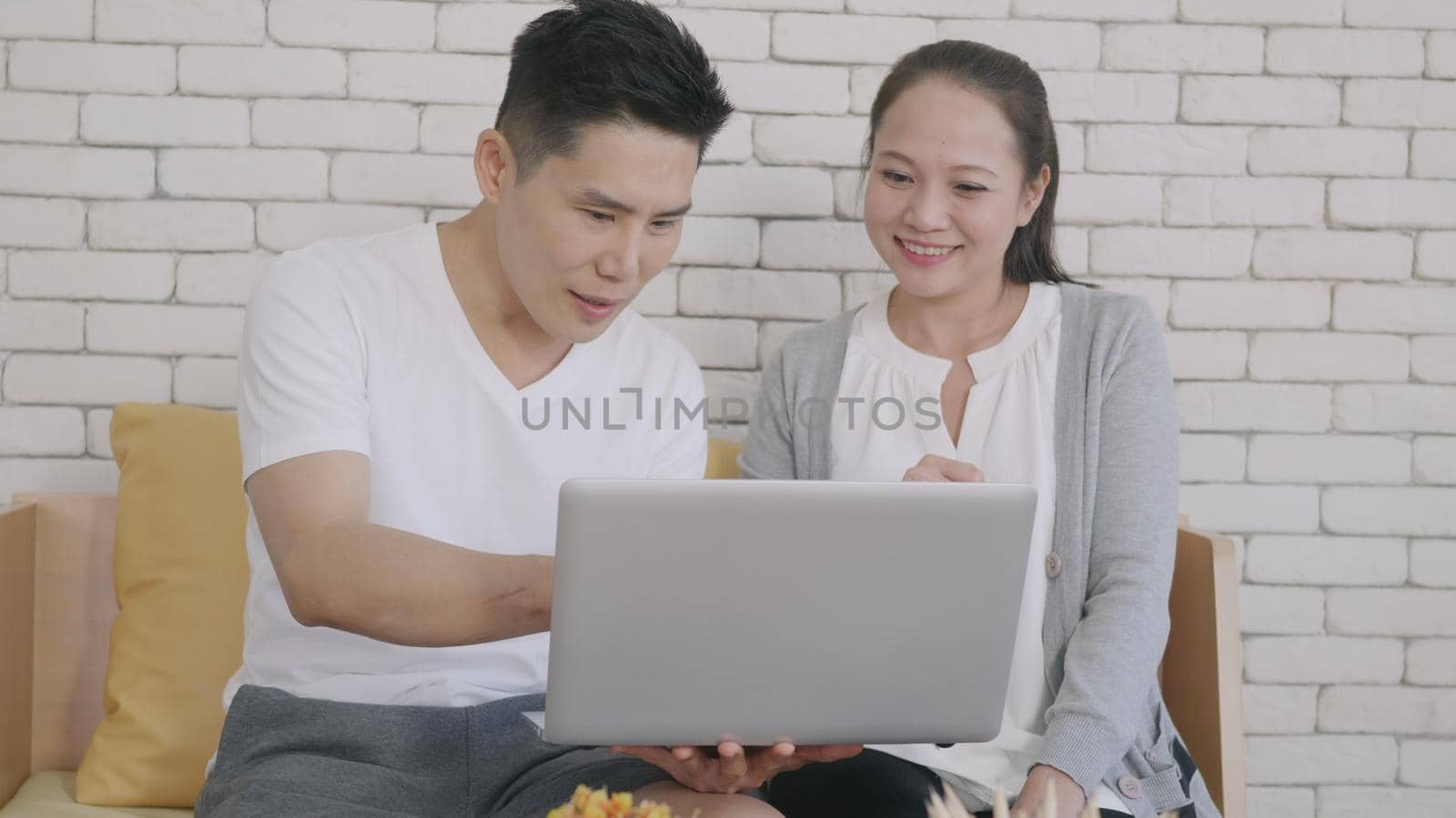 Happy Asian family couple husband and wife work and using laptop computer analyzing their finances discuss. Cheerful loving couple smile shopping order products online together from home by computer