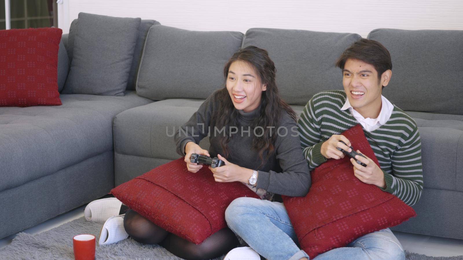Happy Asian beautiful young family couple husband and wife smile and laugh enjoying funny with each other playing video game, holding joysticks console. Happiness and gaming concept.