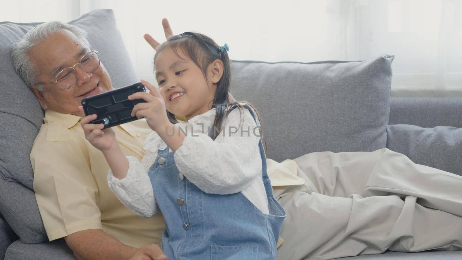 Happy senior grandfather with grandson taking photo by smartphone, old grandpa embracing little grand child take selfie on mobile phone together sit on sofa in living room at home, elderly and kid