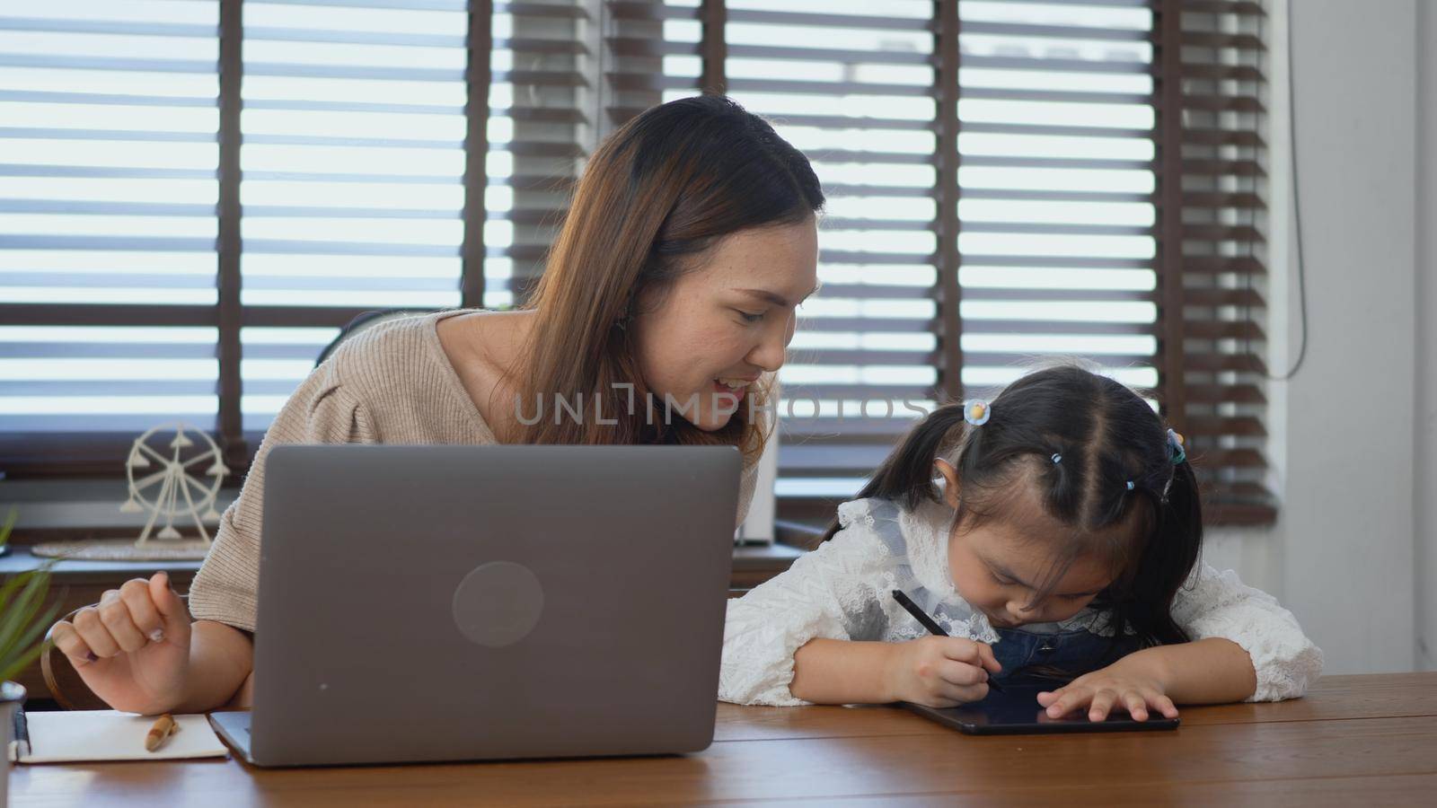 Asian young mother working with laptop computer at home and help daughter doing homework, Single mom freelancer work from home and helping his girl kid teaching homework on desk