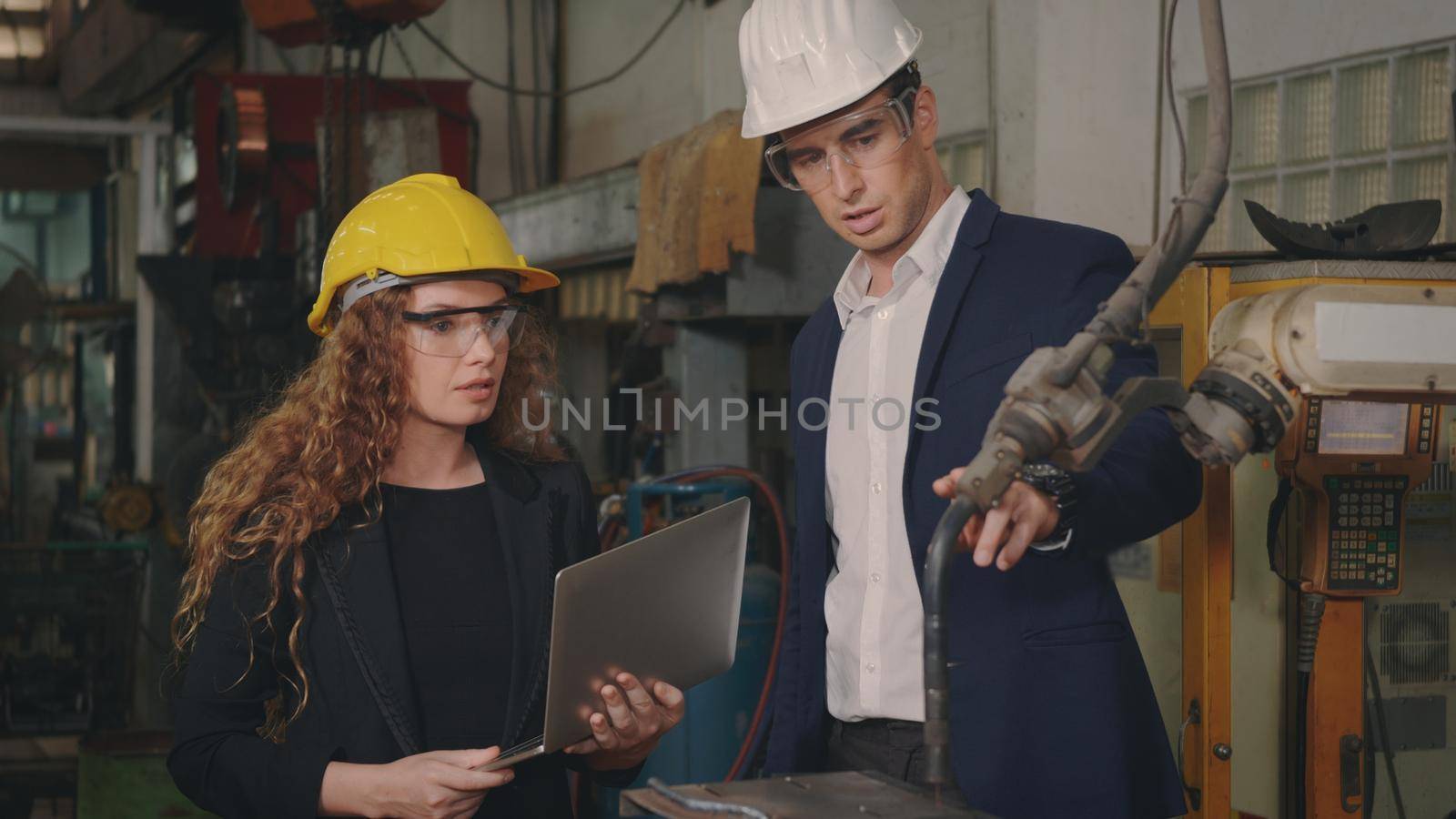 Caucasian maintenance engineer man and diverse female factory workers in hardhats talking and present or explain robot welding machine on plant, Manager supervisor and industrial manufacturing