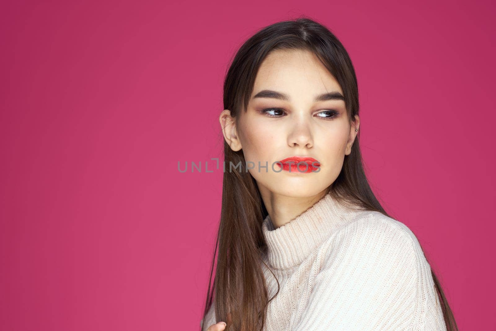 Brunette with long hair red lips cosmetics white sweater pink background cropped view. High quality photo